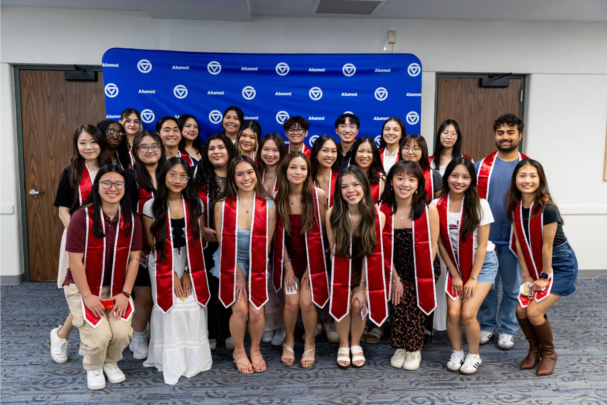 Asian Grad Celebration students in a group photo with red stolls and a GVSU background.